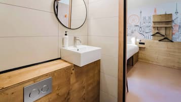 Un baño moderno con un tocador de madera, un espejo redondo, un lavamanos blanco y una pared con un mural de un paisaje urbano.