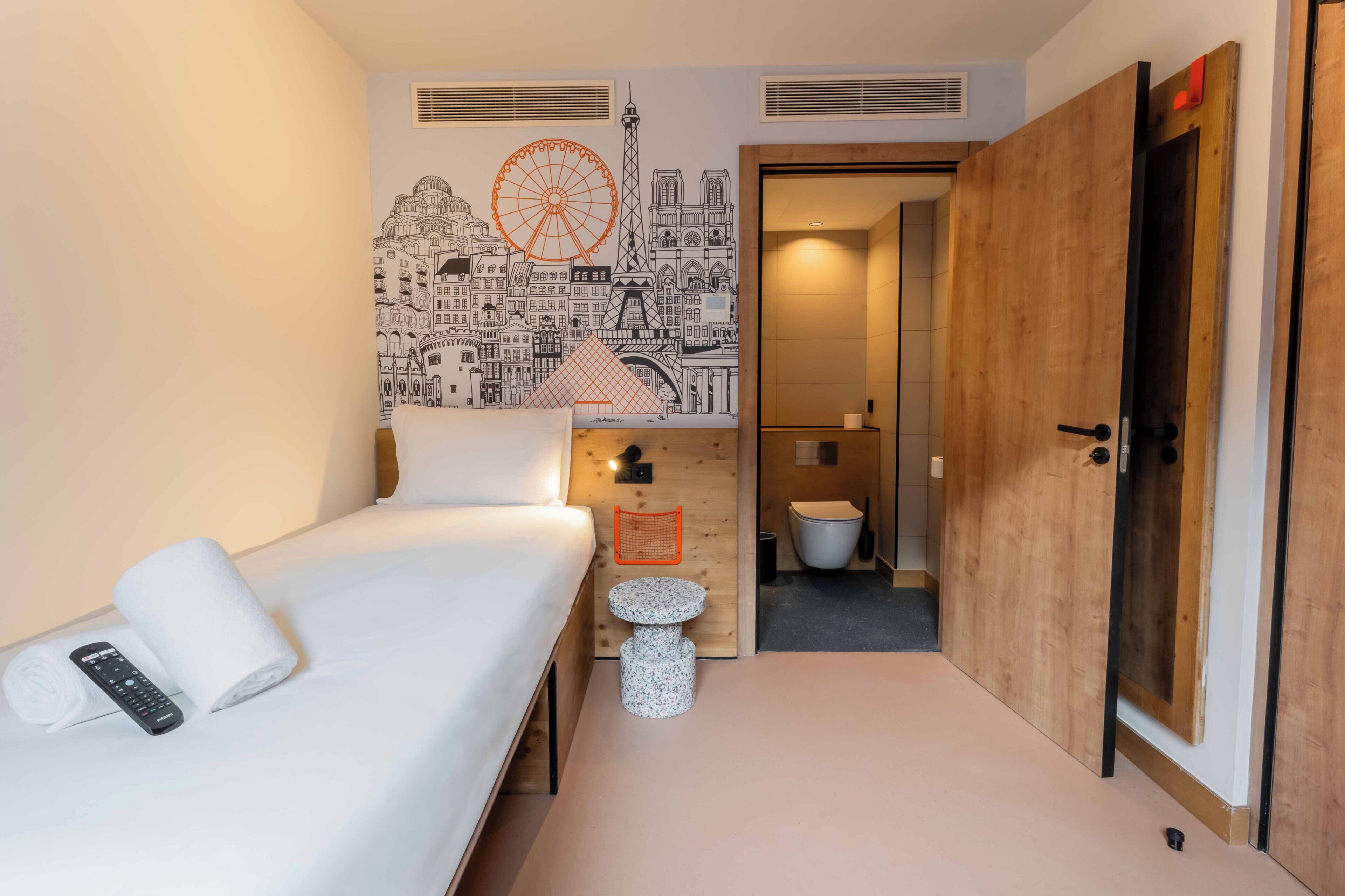 Una habitación de hotel con cama, un mural en la pared, una mesita redonda y una puerta de madera.