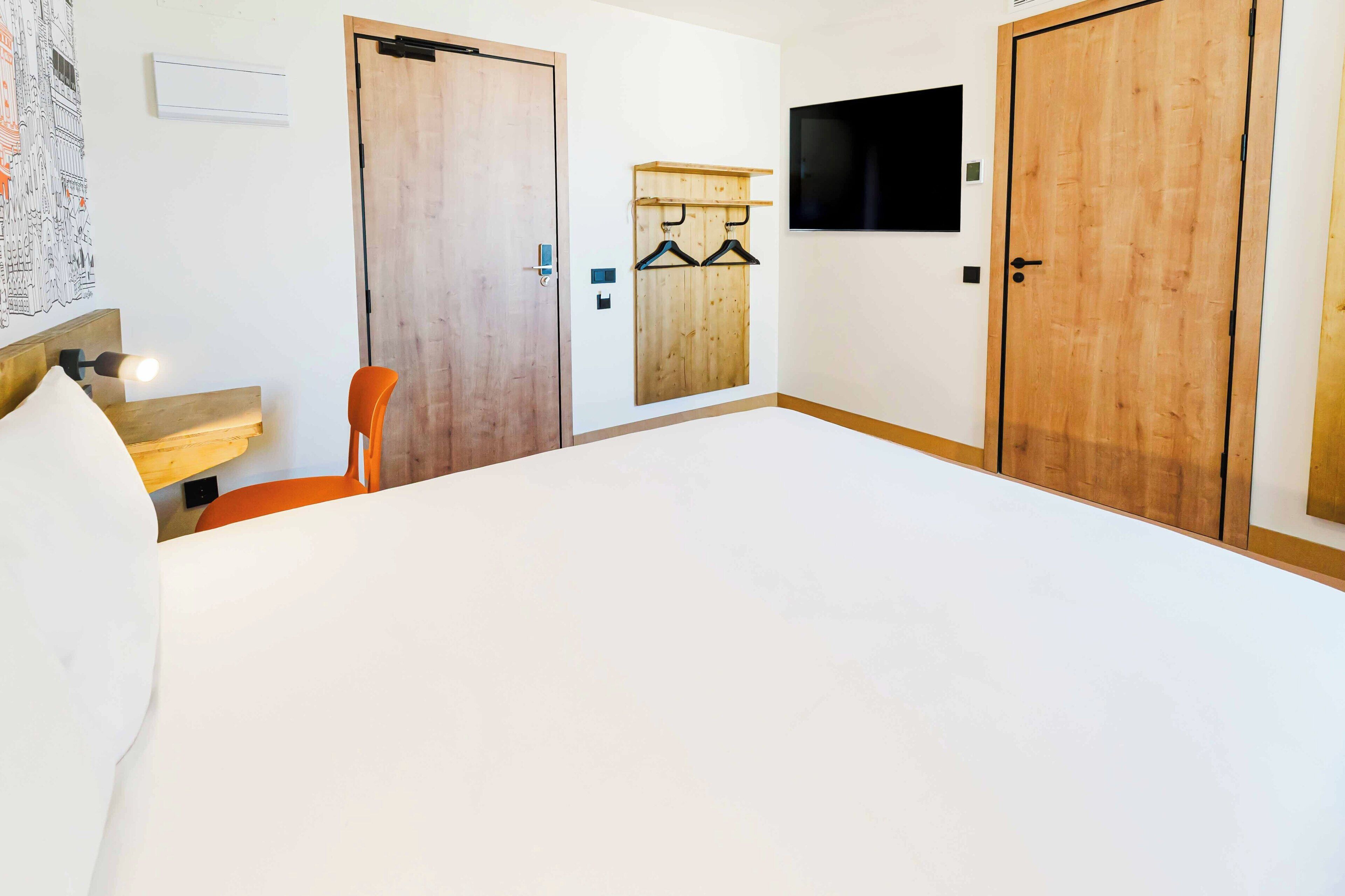 Een hotelkamer met een groot bed, een stoel, een aan de muur bevestigde televisie en houten deuren.