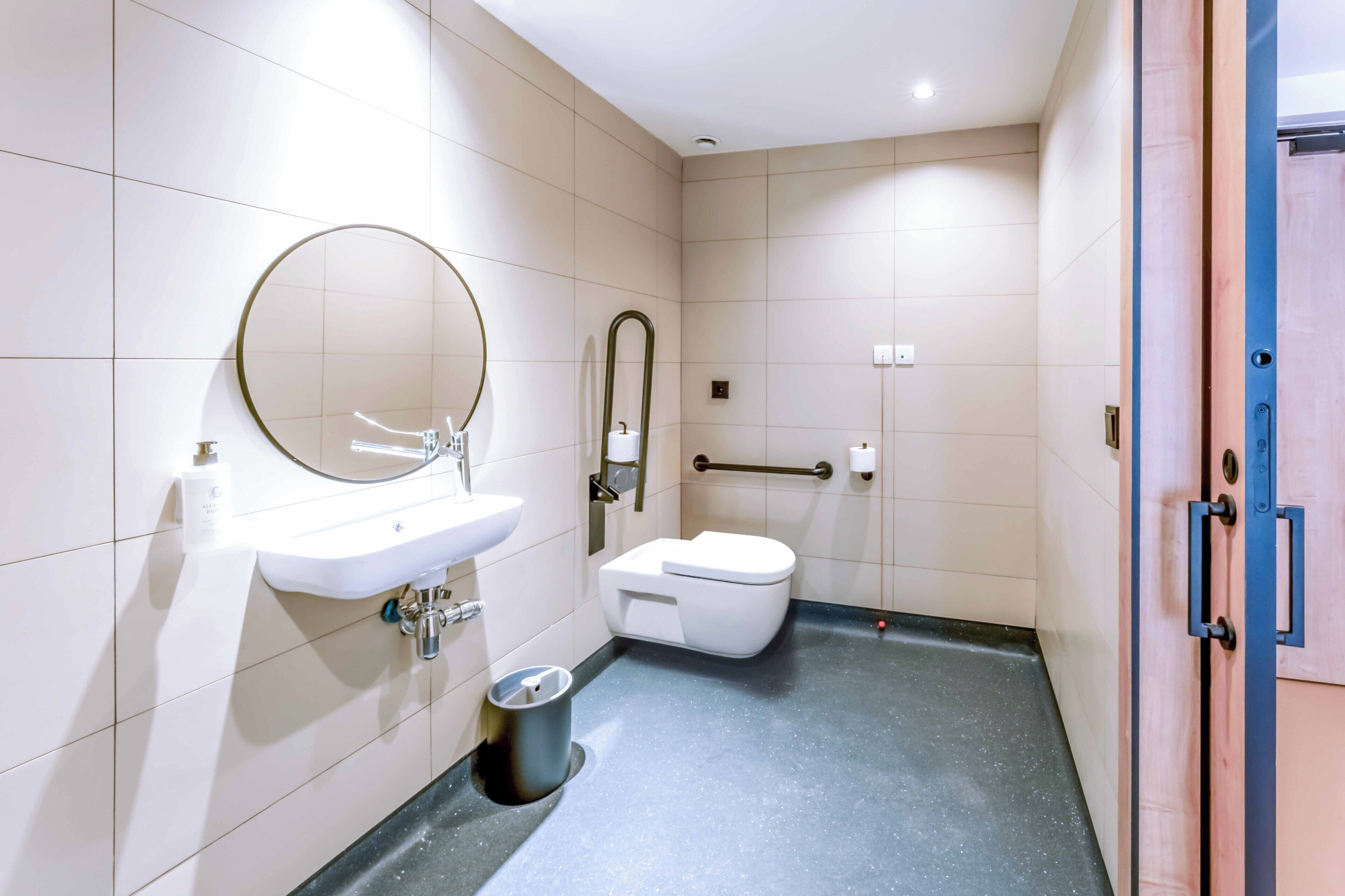 Un baño moderno con lavamanos, espejo, inodoro y barra de apoyo.