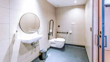 Un baño moderno con lavamanos, espejo, inodoro y barra de apoyo.