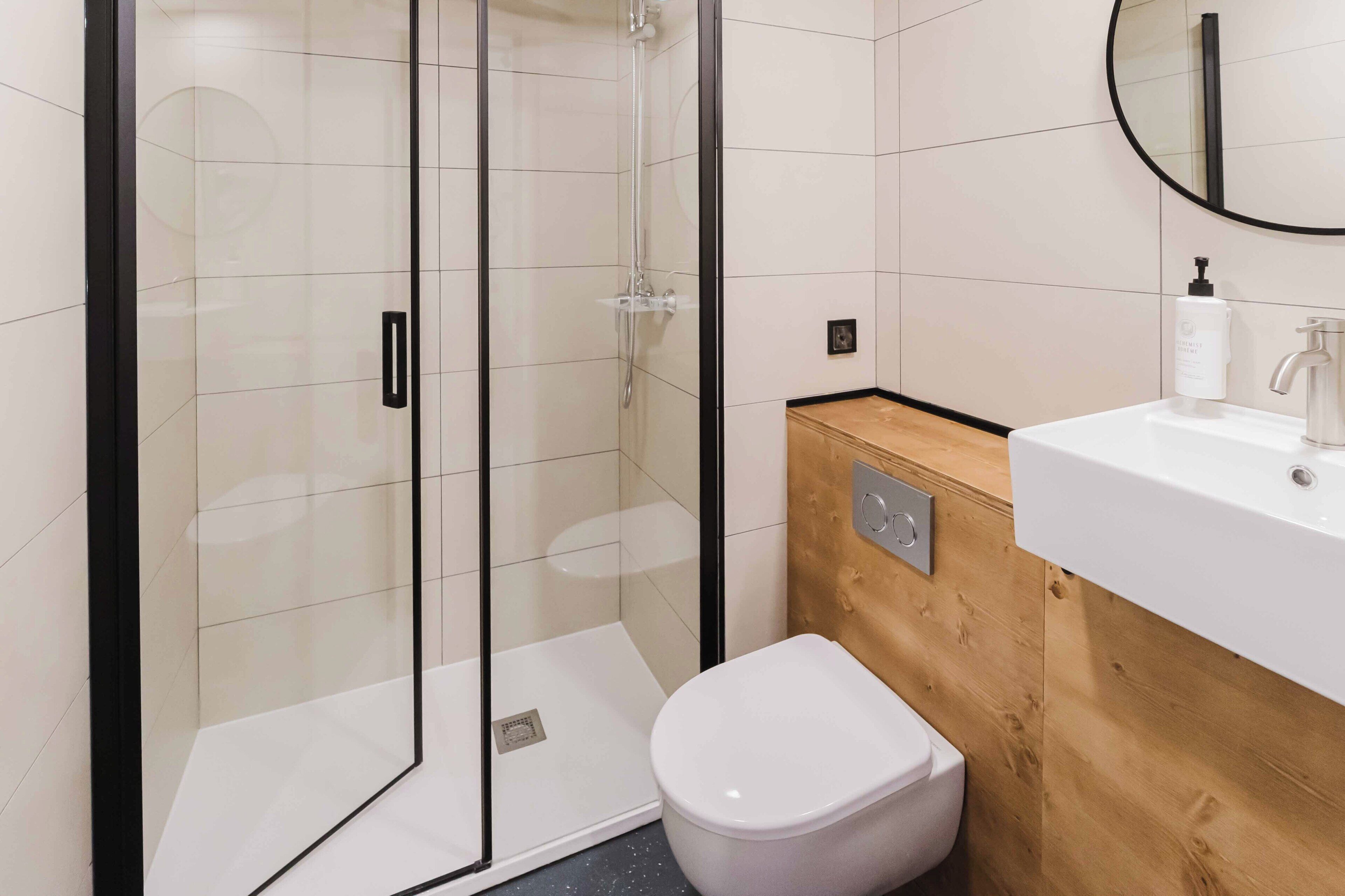 Een moderne badkamer met een douchecabine van glas, een wit toilet en een houten wastafelmeubel met een wastafel.