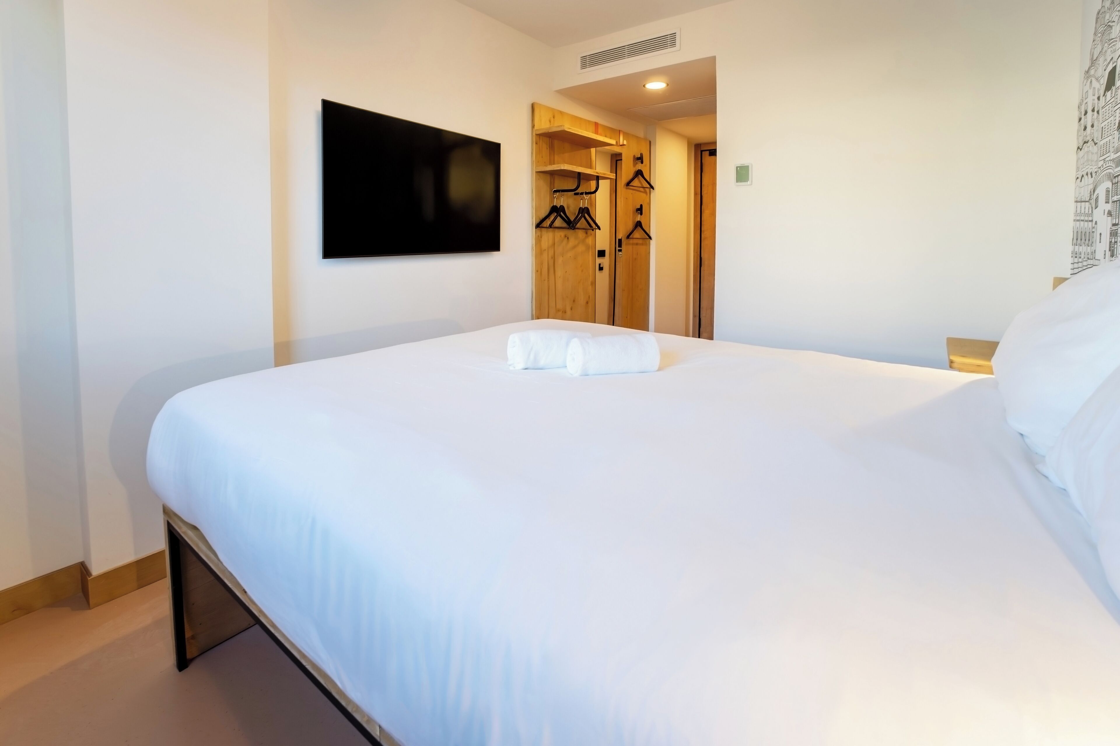 Une chambre d’hôtel avec un grand lit, un téléviseur à écran plat fixé au mur et une armoire en bois dotée d’un miroir.