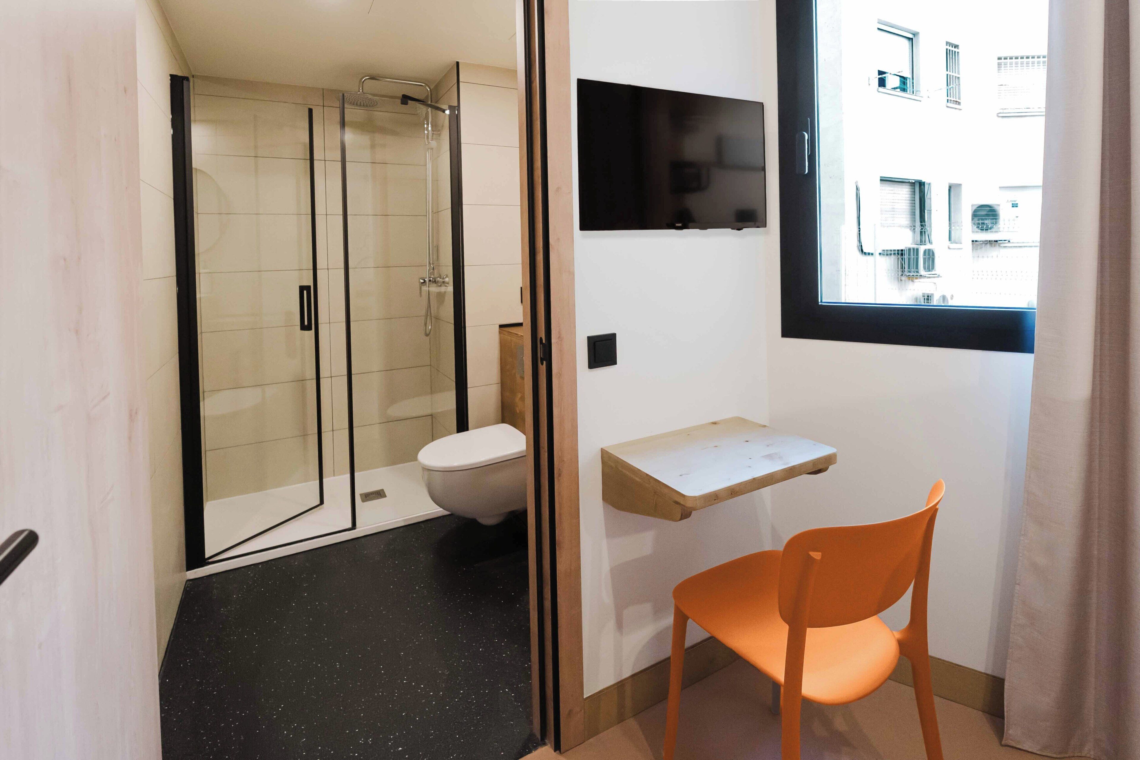 Baño con ducha, inodoro y un pequeño estante de madera.