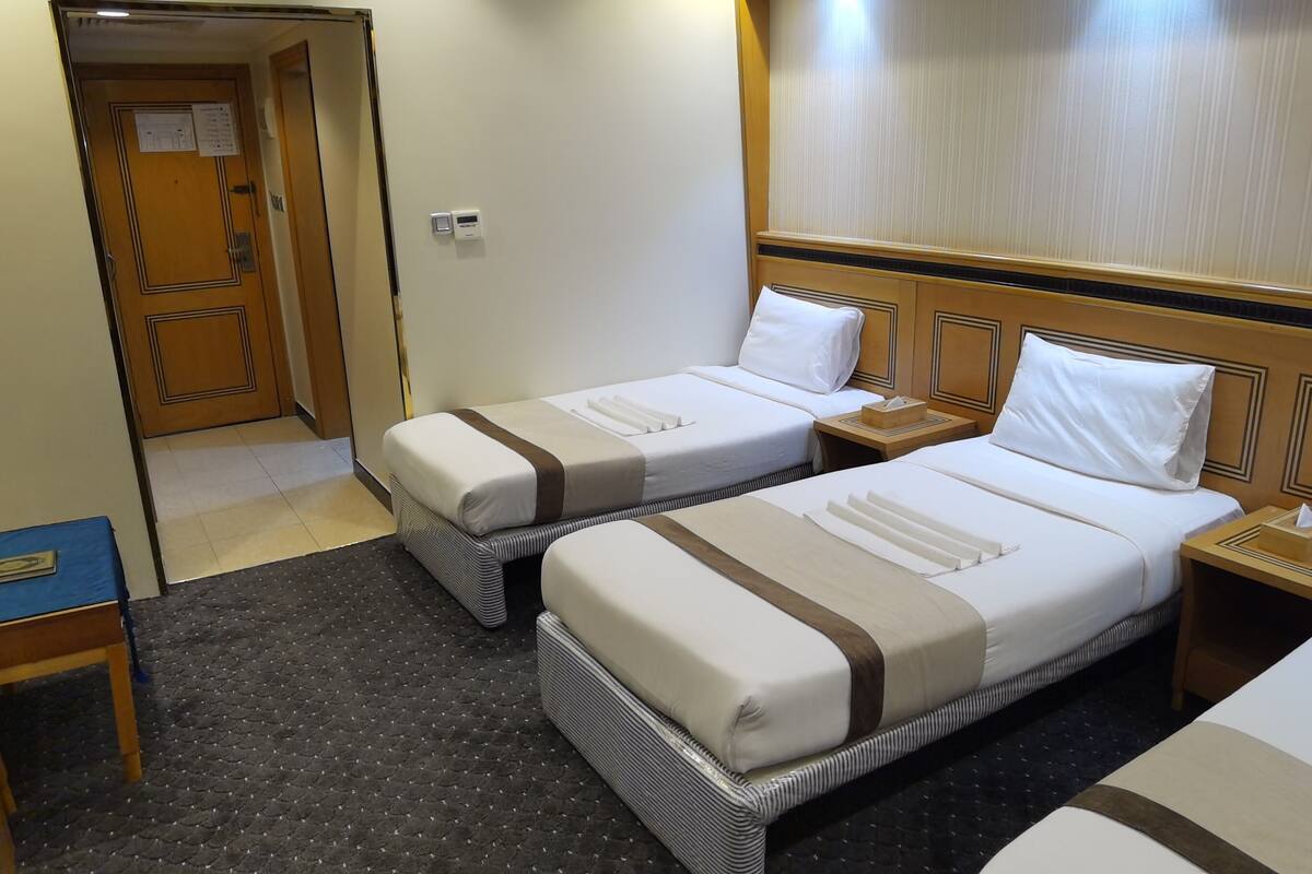 A hotel room with two single beds, a small wooden table, a blue folder, and a door leading to another room.