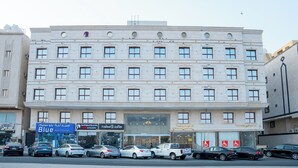 A multi-story building with several ground-floor shops, including a pharmacy and a vision center. - Jana Al Beet Hotel By Orvana (Makkah)