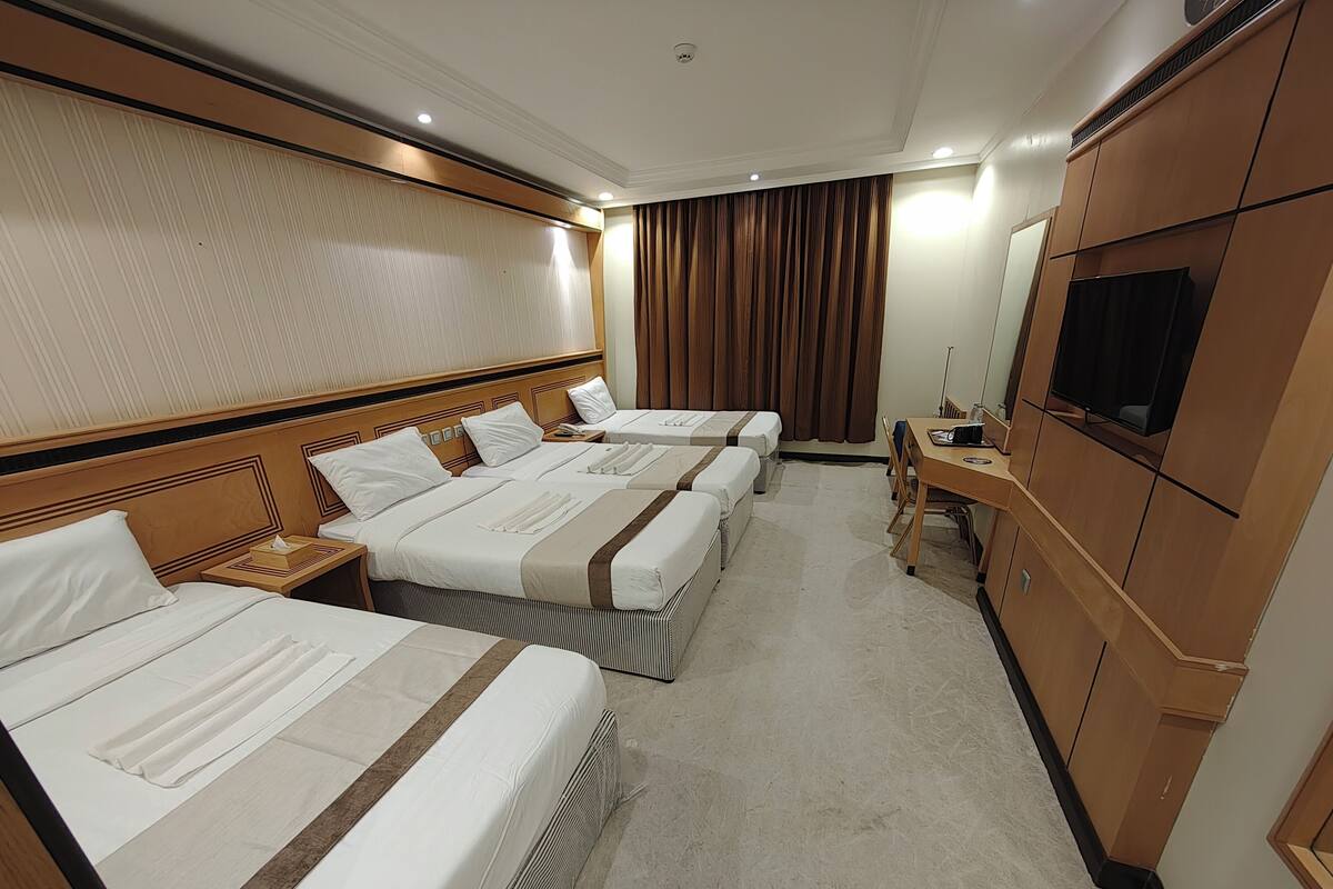 A hotel room with three beds, a TV, a desk, and a mirror.