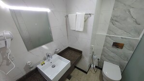 A bathroom with a white sink, a mirror, a hairdryer, a towel rack, a shower, and a toilet. - Jana Al Beet Hotel By Orvana (Makkah)