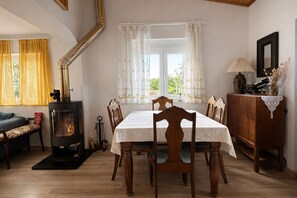 A cozy dining area with a table set for four, a wood-burning stove, and a view through the window.