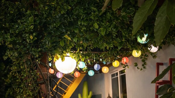 Un espacio exterior acogedor con terraza de madera, una silla acolchada, una mesita y un farol decorativo.