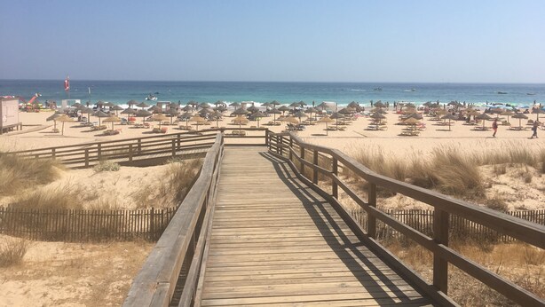 Un camí de fusta que condueix a una platja amb ombrel·les i gandules.
