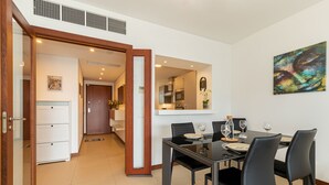 Una zona de menjador moderna amb una taula de vidre, cadires negres i una cuina al fons.