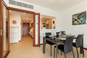A modern dining area with a glass table, black chairs, and a kitchen in the background. - Apartment - Near beach - Swimming pool - Garden view - Lagos (Lagos)