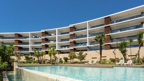 Hotel de diversos pisos amb piscina, seients de relaxació a l'aire lliure i palmeres.