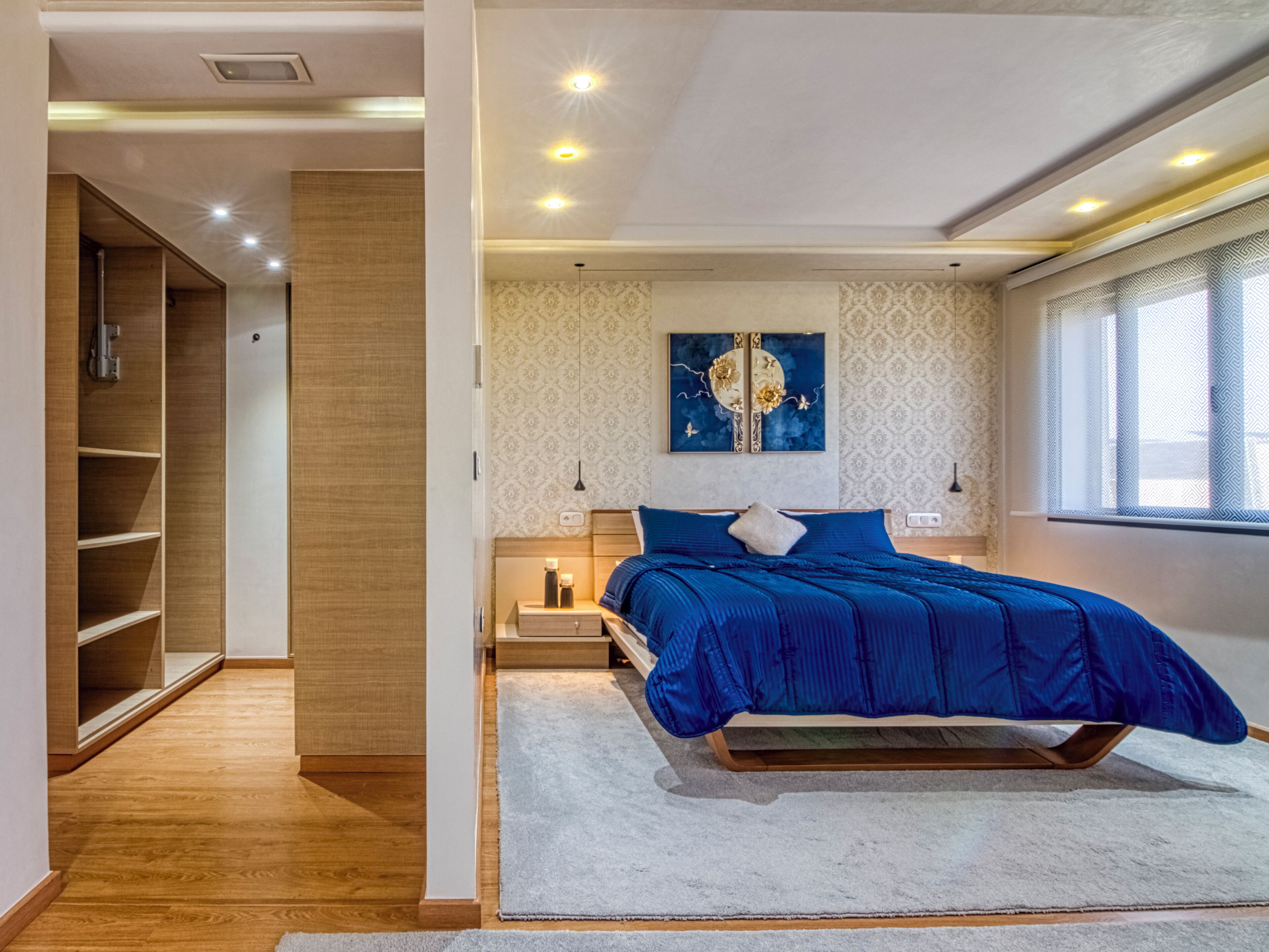 A modern bedroom with a bed, bedside tables, a nightstand, a wardrobe, and a window with curtains.