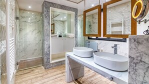 Een moderne badkamer met marmeren wanden, een ruime douche en twee wastafels.