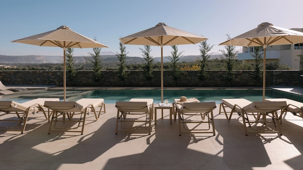 Zona piscina con lettini e ombrelloni, un muro in pietra e vista sulle montagne.