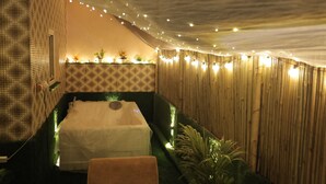 A room with a bed, string lights, and a bamboo wall.
