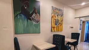 Een eethoek met twee tafels en vier stoelen, een plafondlamp en twee schilderijen aan de muur.