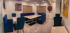 A dining area with a long table and blue cushioned booths, air conditioning units on the walls, and artwork on the walls. - C & C Luxury Suites (Lagos)