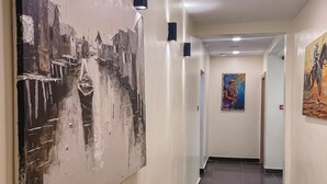 Een gang met een groot abstract schilderij links, een kleiner schilderij rechts, en een betegelde vloer.
