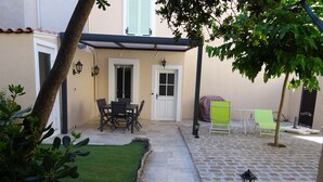A courtyard with a dining table and chairs, a covered seating area, and a small garden with artificial grass.