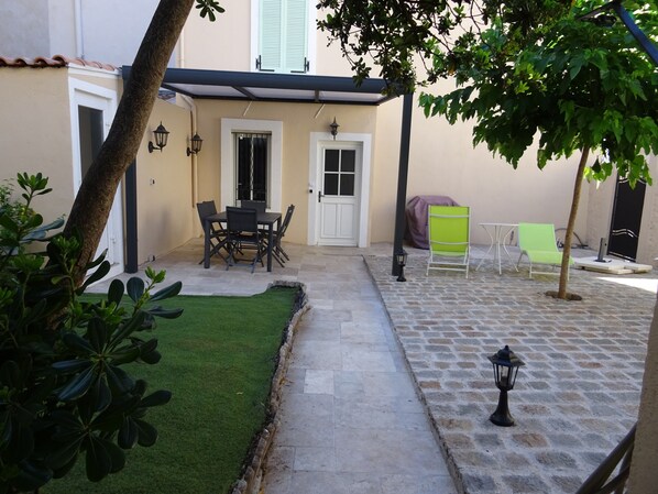A courtyard with a dining table and chairs, a covered seating area, and a small garden with artificial grass.