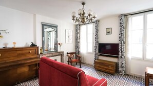 A room with a red sofa, wooden dresser, TV, patterned floor, and a chandelier.