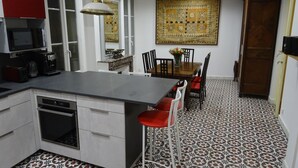 A kitchen with a central island, bar stools, a dining table with chairs, a microwave, a coffee maker, and a patterned floor.
