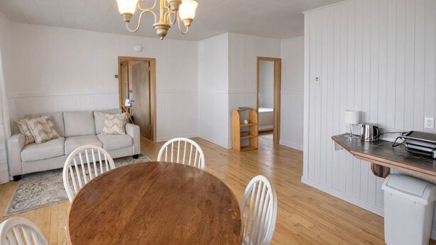 Una sala de estar moderna con una mesa de comedor de madera, sillas blancas, un sofá color beige y una lámpara de araña.