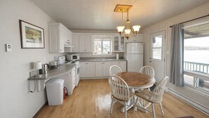 Cocina moderna con armarios blancos, una mesa de comedor de madera y vista a una masa de agua a través de amplios ventanales.