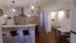 A kitchen with a tiled backsplash, a microwave, and a stove. There are two bar stools and a table with chairs. - City Center Forcalquier Apartment with Balcony (Forcalquier)