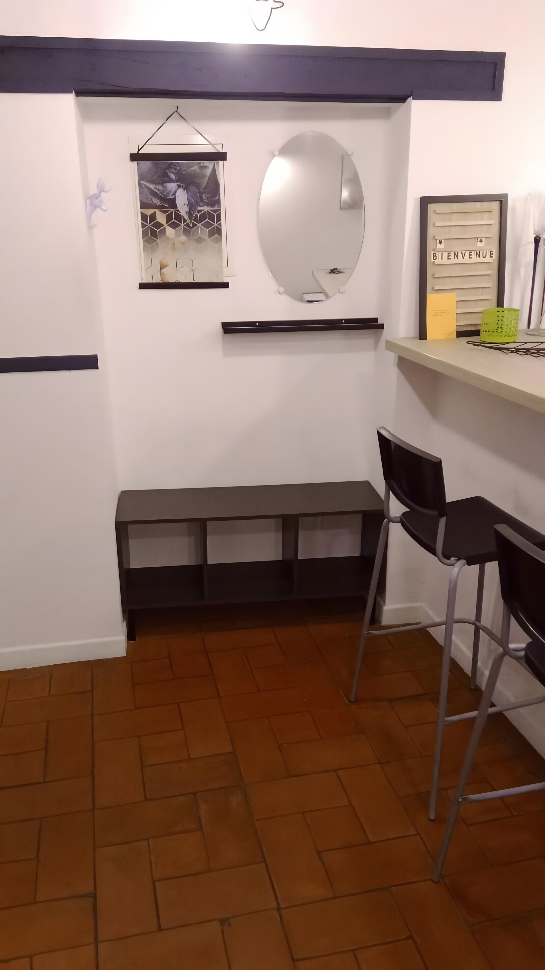 A small, enclosed room with a bench, a chair, a mirror, a welcome sign, and a shelf with items.