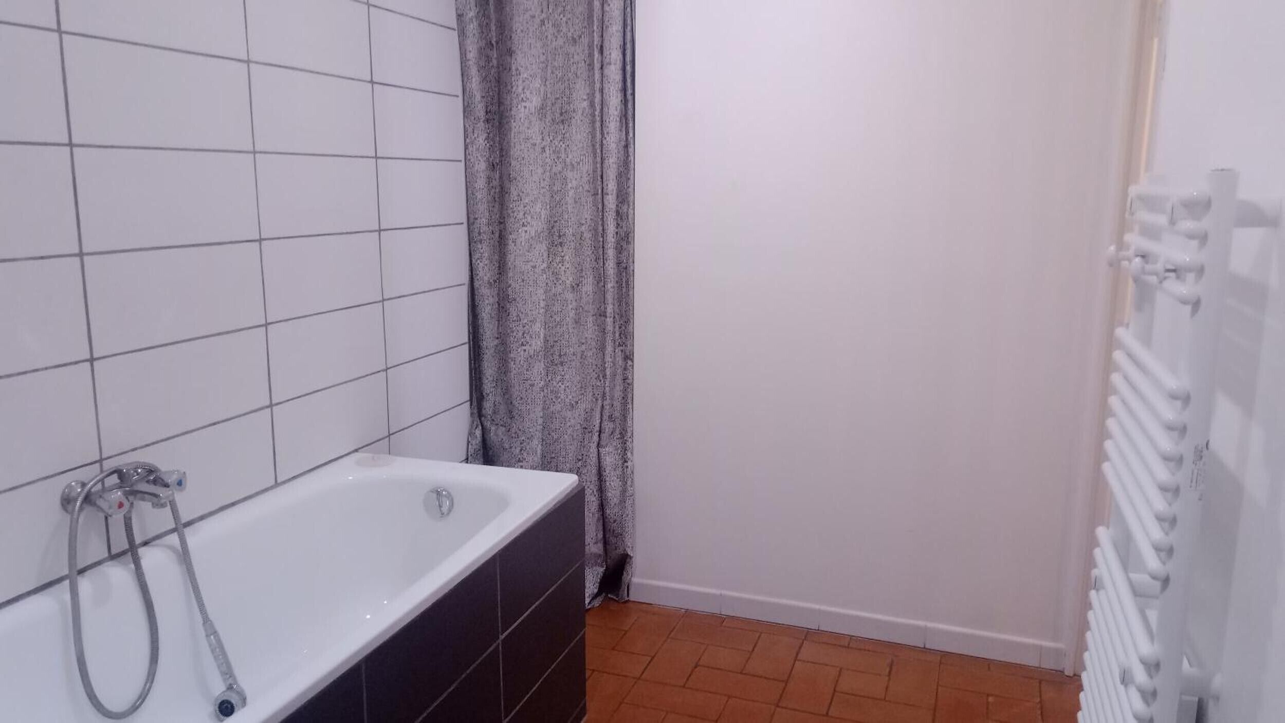 A bathroom with a bathtub, a shower, tiled walls, and a radiator.