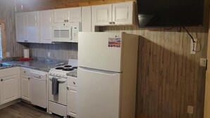 A kitchen with white cabinets, a microwave, an LG refrigerator, a stove, and a ceiling fan. - Tiny cabin on 10 acres with pond (Albertville)