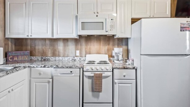 A kitchen with white cabinets, a microwave, a stove, a dishwasher, and a refrigerator. - Tiny cabin on 10 acres with pond (Albertville)