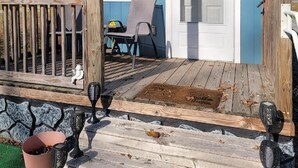 A blue house with a porch, a door, and a small table with chairs. - Tiny cabin on 10 acres with pond (Albertville)