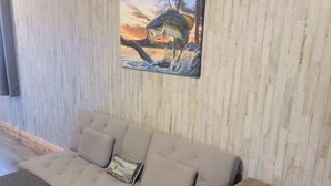 A modern living room with a grey sofa, a wooden coffee table, and a painting of a fish jumping out of water. - Tiny cabin on 10 acres with pond (Albertville)