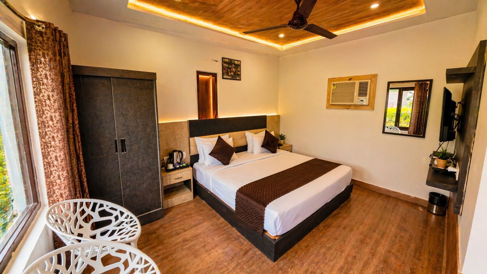 A hotel room with a bed, a desk, a chair, a wardrobe, a ceiling fan, and a window.