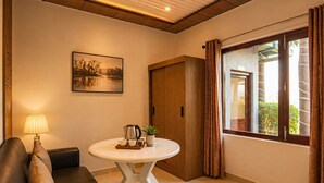 A cozy room with a round table, a sofa, a painting, and a window with curtains. - Jungle Nest Retreat Resort (Ramnagar)