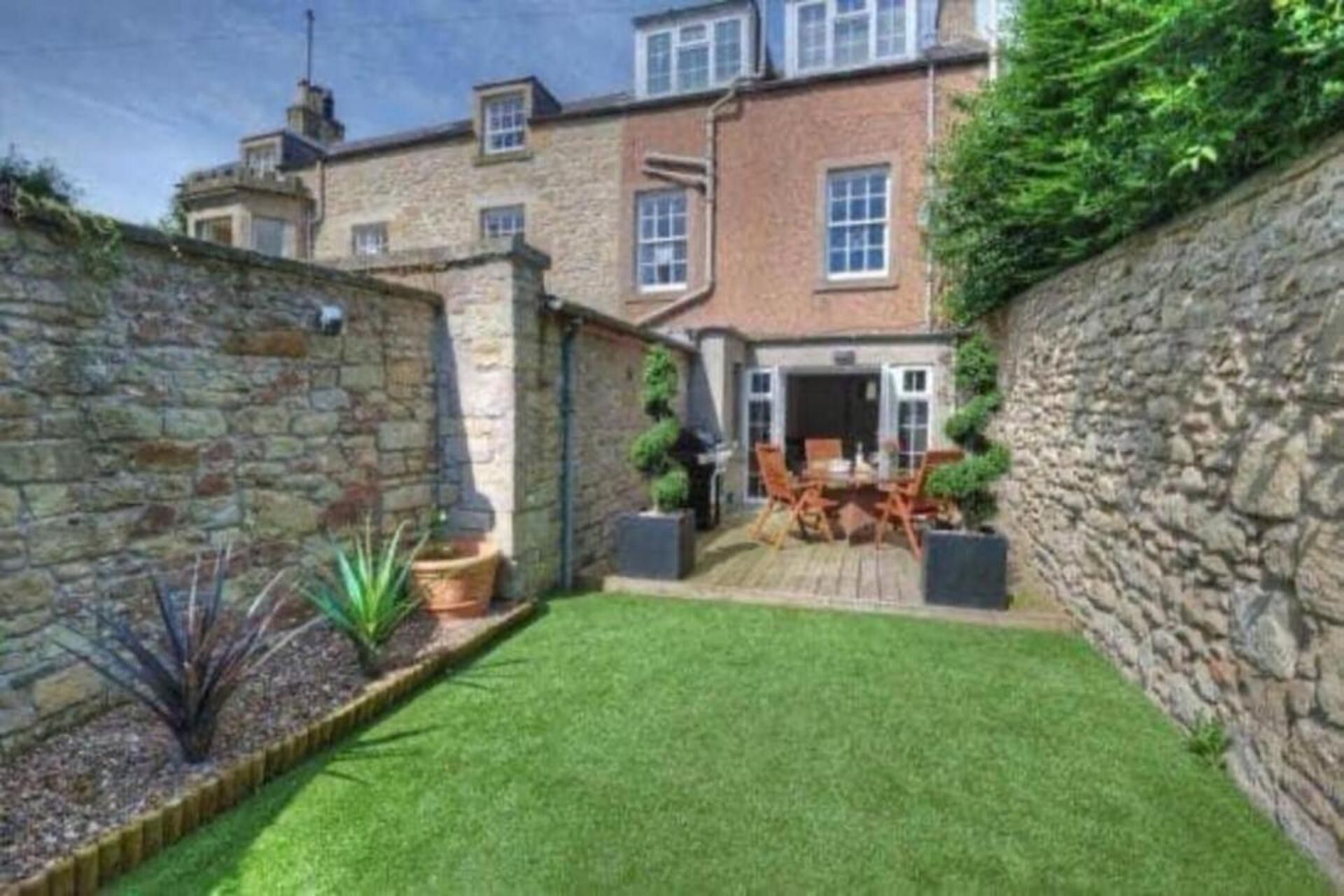 A courtyard with a lawn, a patio area with chairs, and a stone wall.