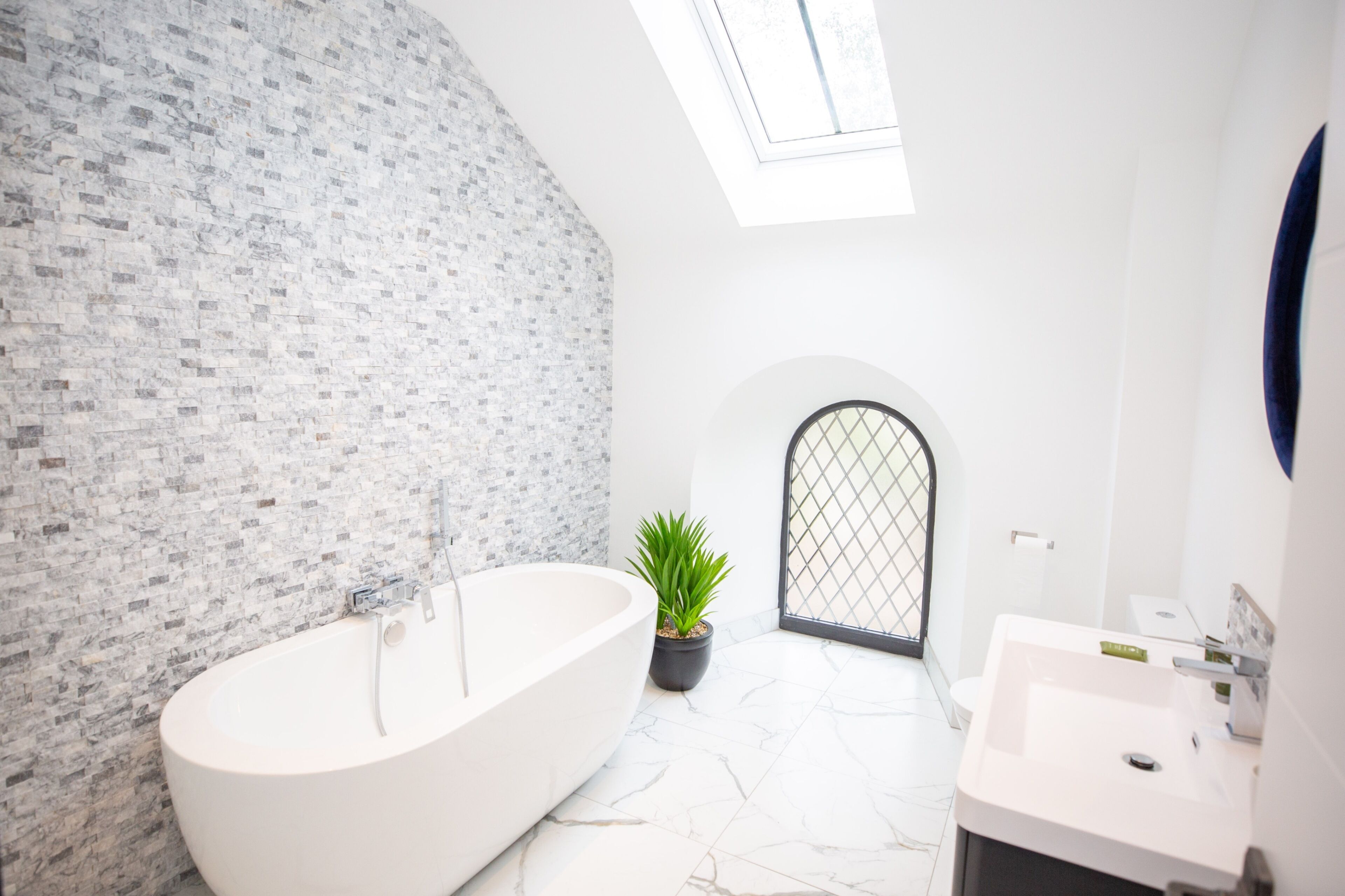 A modern bathroom with a freestanding bathtub, a sink, and a potted plant.