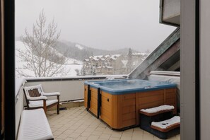 Een bubbelbad op een balkon met uitzicht op een besneeuwd landschap en gebouwen.