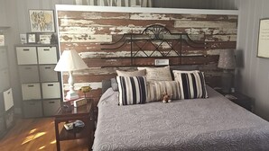Ein Schlafzimmer mit einem rustikalen Holz-Kopfteil, einem Bett mit gestreiften Kissen, einem Nachttisch mit einer Lampe und einem Beistelltisch mit einer Uhr.