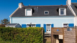 Ein zweistöckiges Haus mit blauer Fassade, einem kleinen Fenster und einer Tür mit blauem Fensterladen.