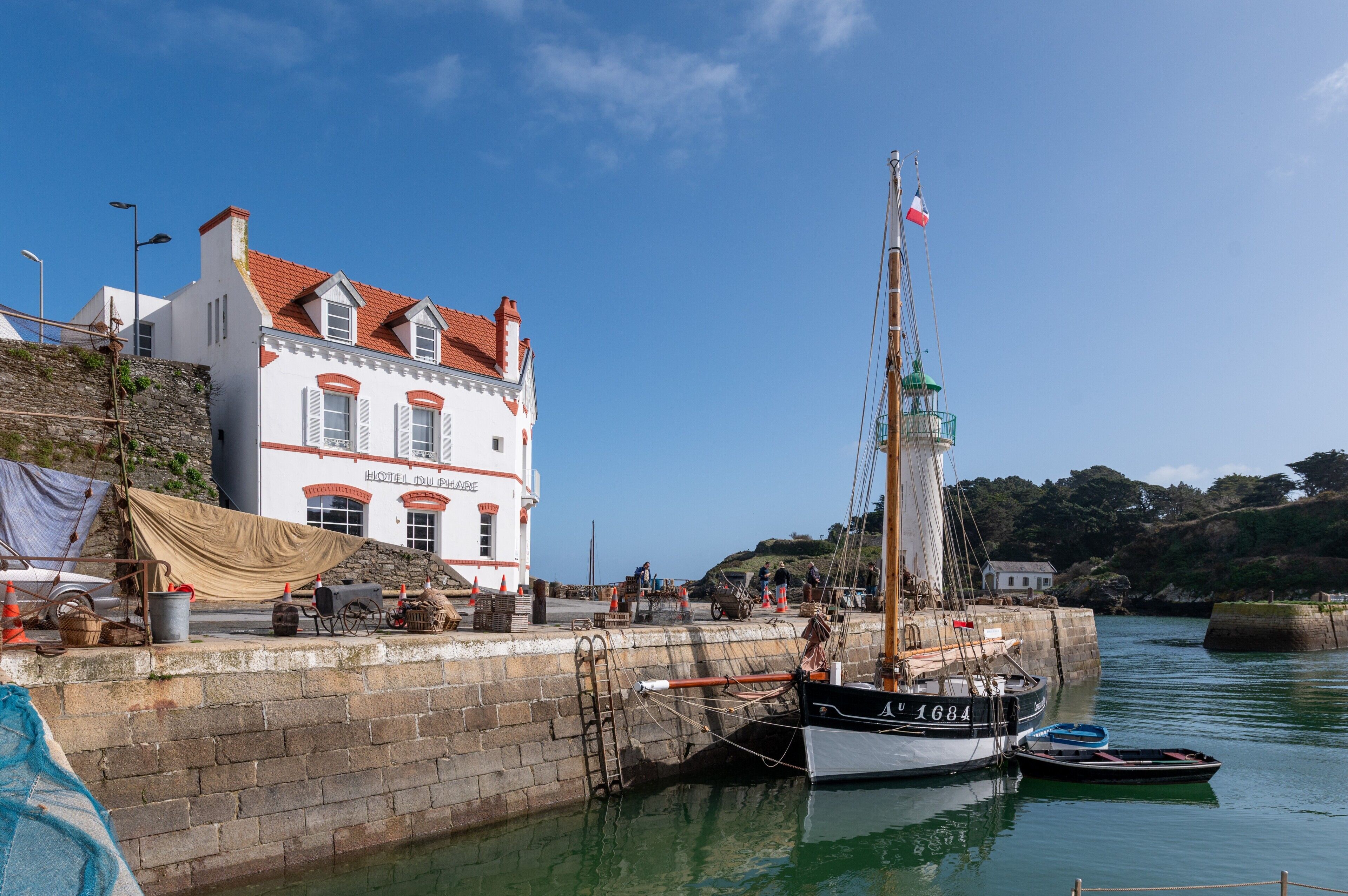 A coastal building with a red roof, a flag, and a sailboat docked nearby.