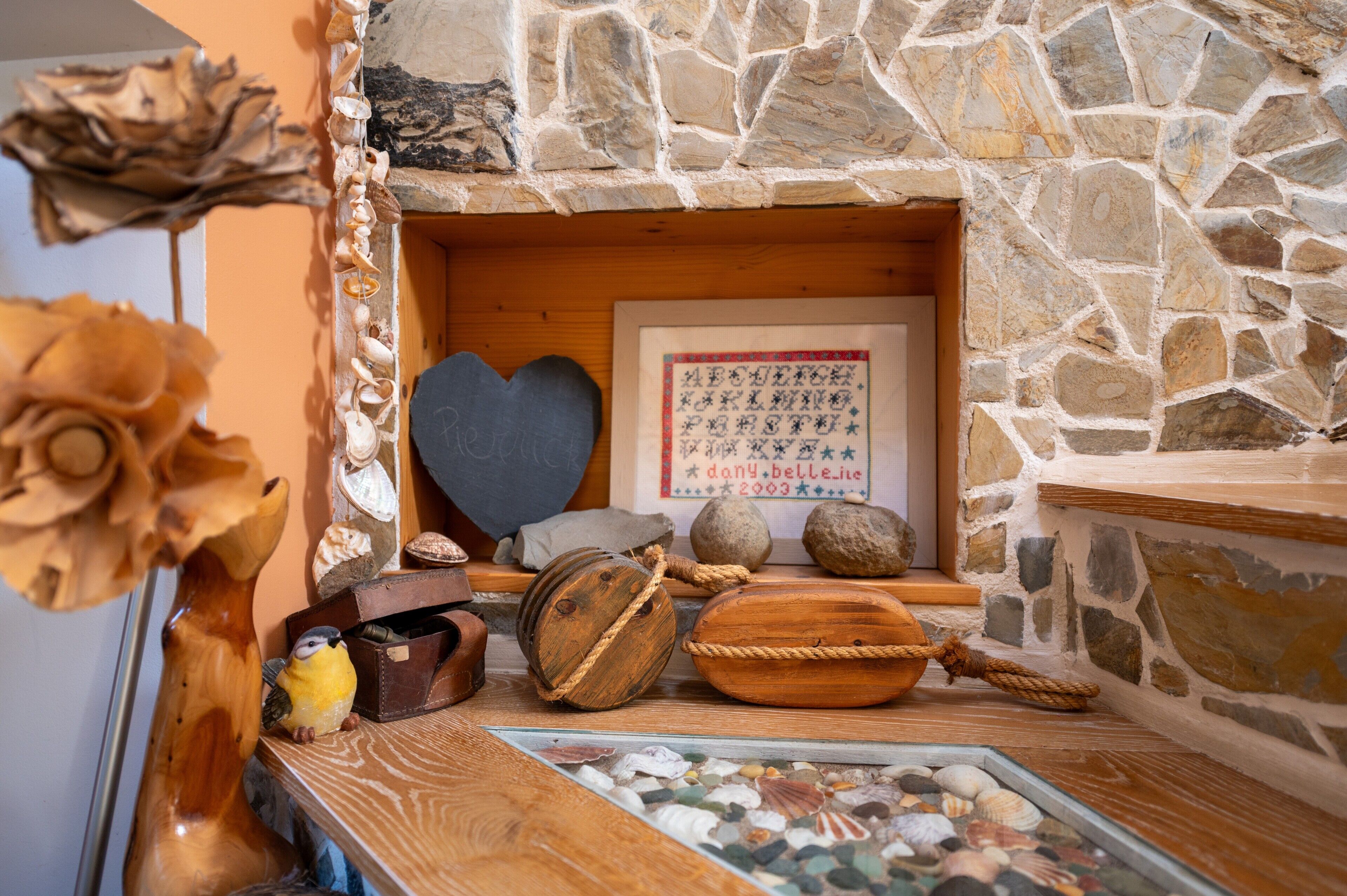 Una chimenea de piedra con un cuadro enmarcado, conchas decorativas y una jaula de pájaro de madera.