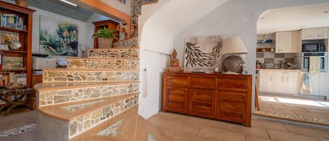Un vaste espace de vie agrémenté d’un escalier en pierre, de meubles en bois et d’une cuisine située au fond de la pièce.