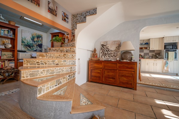 A spacious living area with a stone staircase, wooden cabinets, and a kitchen in the background.