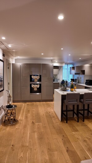 Une cuisine moderne dotée d’appareils électroménagers en acier inoxydable, d’un plancher en bois et d’un coin repas avec des tabourets de bar.